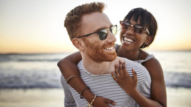 A young heterosexual couple hugging on the beach at sunset.