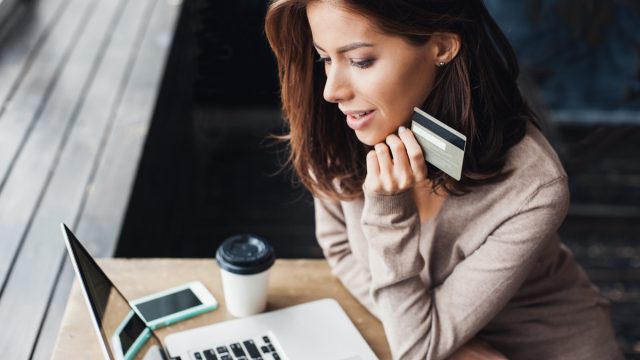 woman holding a credit card and looking at her computer while at a table