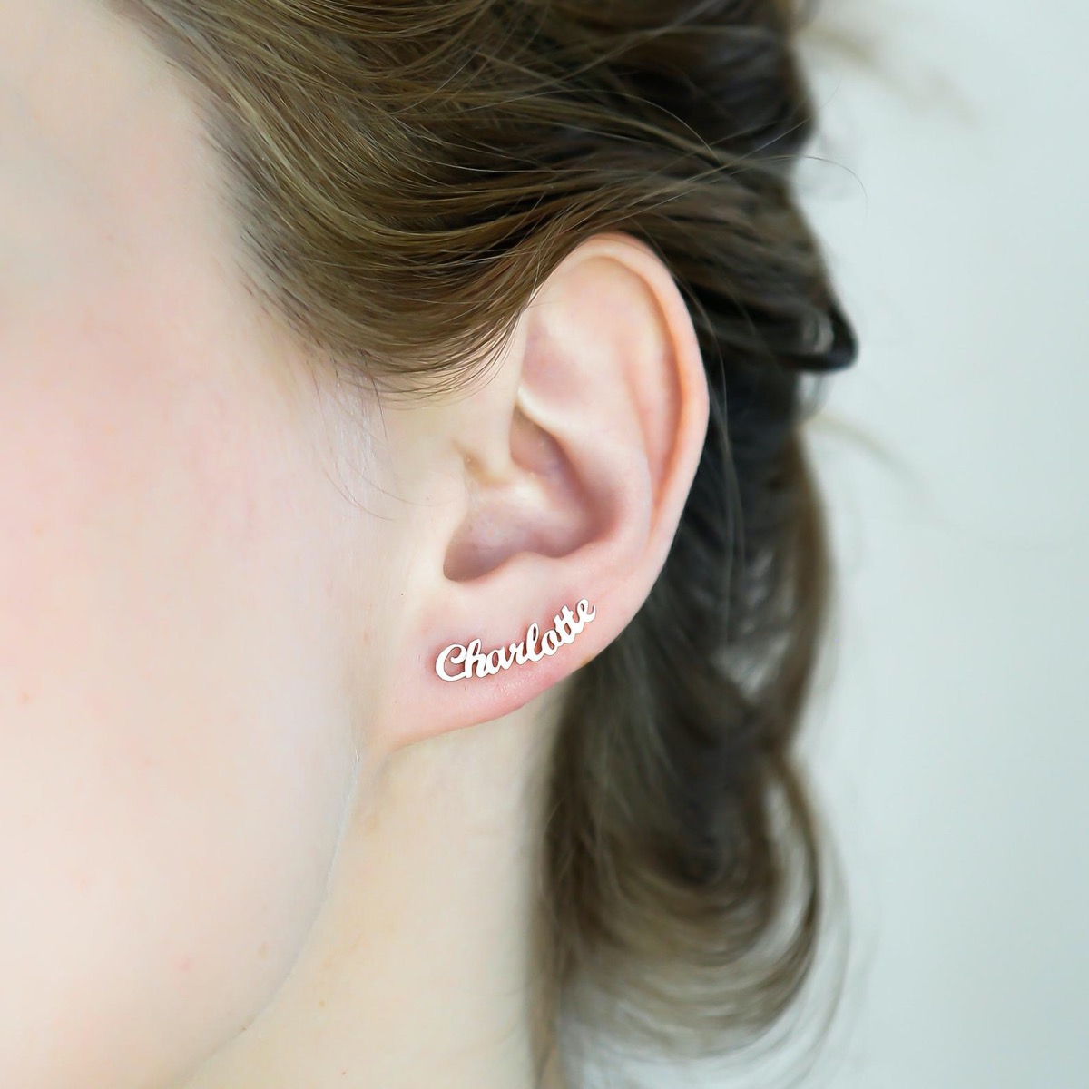white woman with gold earring reading "charlotte" in script in her ear