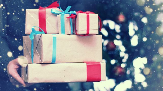 man standing outside holding holiday gifts wrapped in brown paper with colorful bows