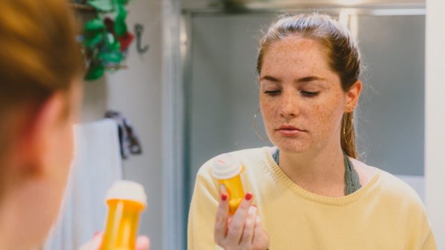 Woman in Bathroom Looking at Pill Bottle