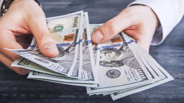 hands counting $100 dollar banknotes on dark wooden surface