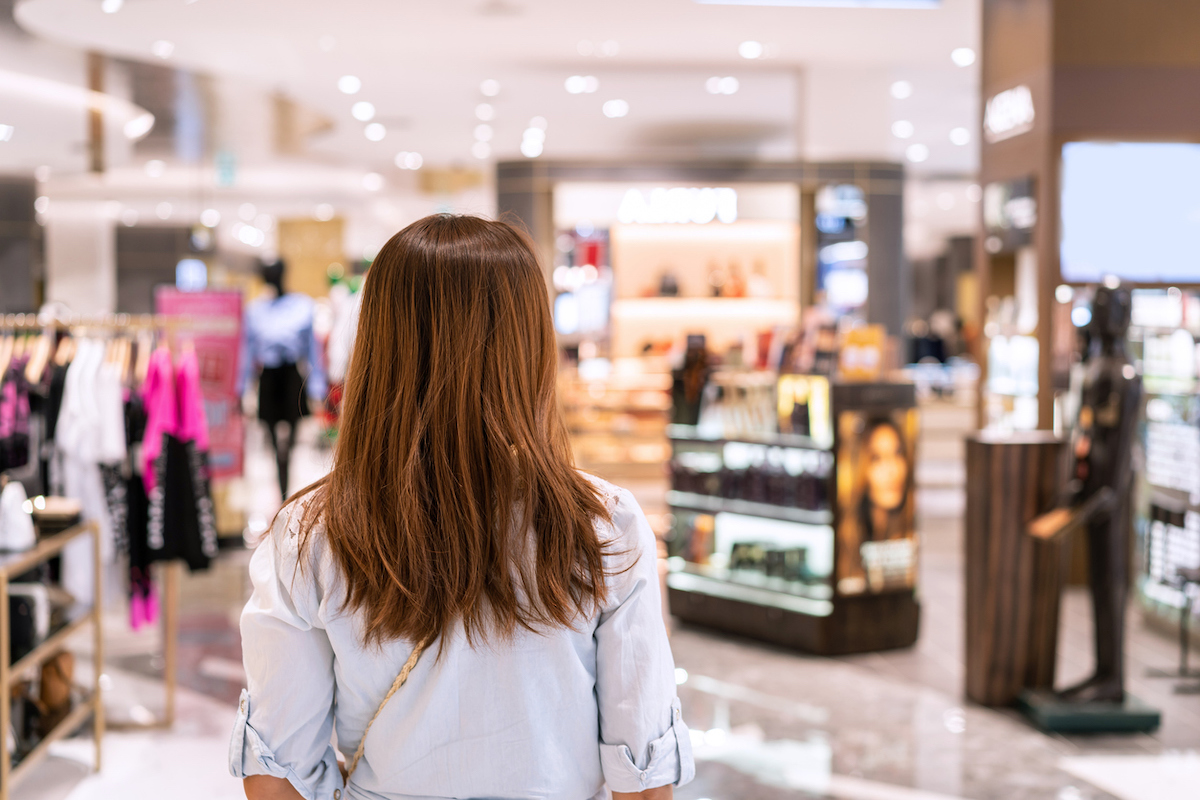 Young woman walking in department store at the mall, photographed from behind