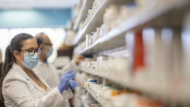 A pharmacist wearing a face mask stocks medicines on a shelf