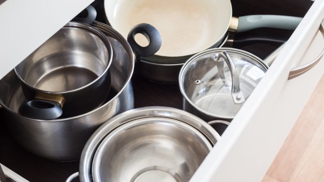 Open drawer of cabinet with steel pots and pans