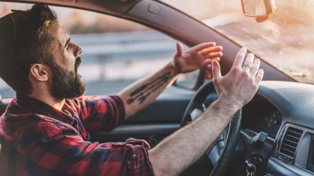 Side view image of irritated young man shouting at other drivers while driving on the highway
