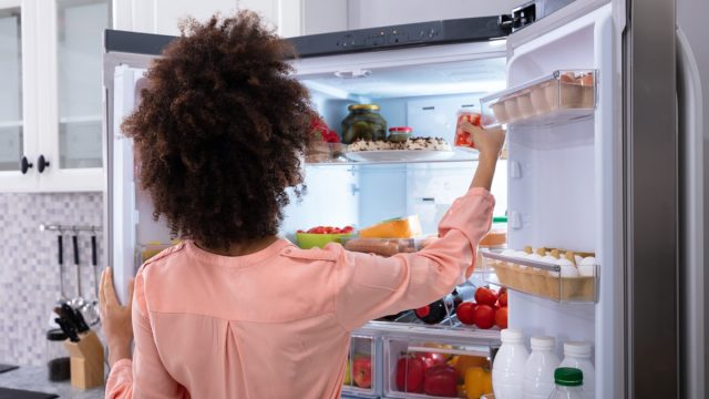 woman in pink shirt with dark curly hair opening double door fridge