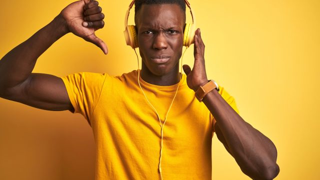 Young man dressed in yellow, listening to music, giving it a thumbs down.