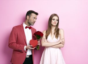 man giving a woman flowers and a heart box and woman looking displeased
