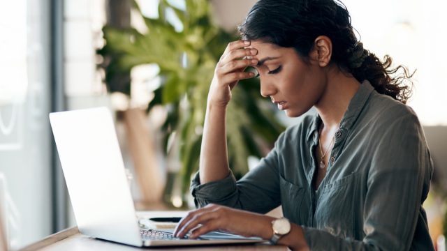 Shot of a young woman experiencing stress while working in a cafe