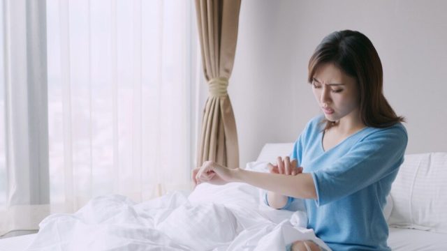 Woman scratching arm in bed from bug bite