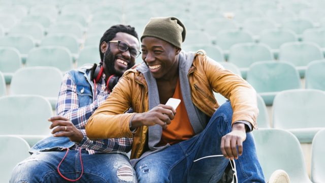 Two young male friends sitting in empty stadium seats laughing