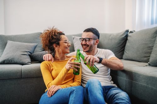 Couple toasting beer bottles at home