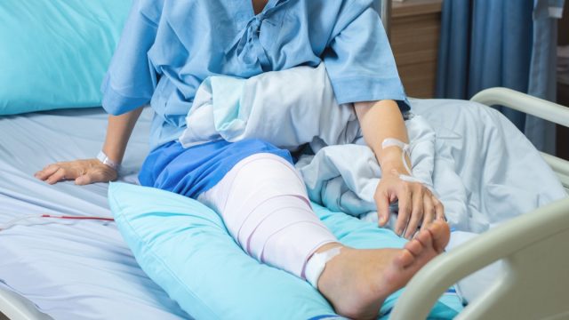 lderly old woman patient lying with bandage compression knee brace support injury on the bed in nursing ward hospital.