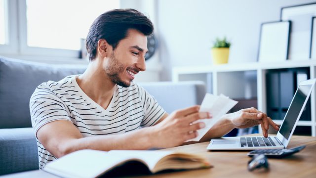 A young man filing taxes on his laptop while smiling and maybe cashing his COVID stimulus check