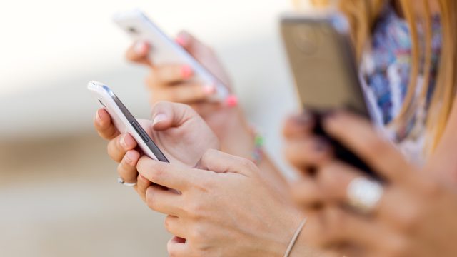 A shot of three people holding smartphones outdoors.