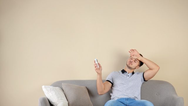 man sweating on couch holding air conditioner remote