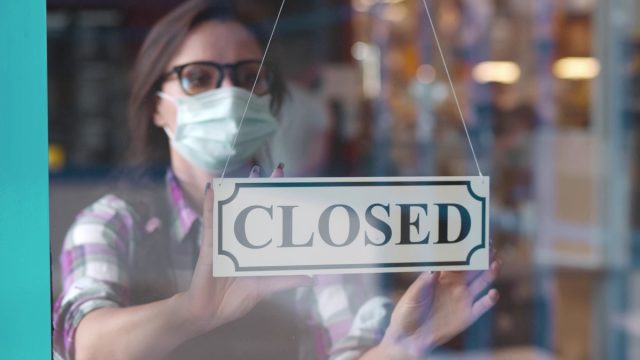 woman in face mask hanging closed sign in restaurant window