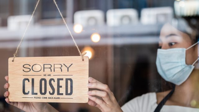 A woman wearing a mask putting up a closed sign on the door of a restauratnt