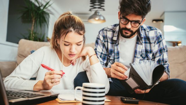 A young man and woman sit on the couch while going over forms to file taxes
