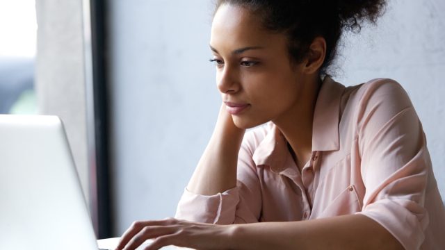woman in her 20s or early 30s using laptop while wearing pink button down shirt