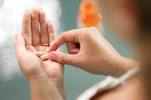 Close up view of young woman holding ginseng vitamins and minerals pills in hand with capsule bottle on table. High angle view