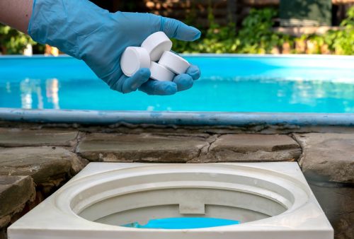 a hand with blue glove putting chlorine in pool