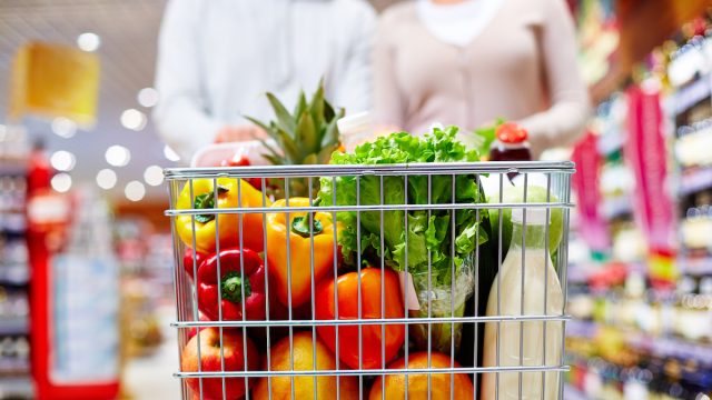 Image of cart full of products in supermarket being pushed by couple
