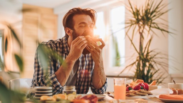 Young man eating sandwich for breakfast at dining table.