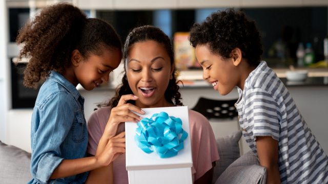 Kids surprising their mother with a gift at home and smiling