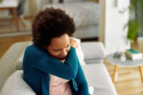 woman coughing into her arm while sitting on the couch
