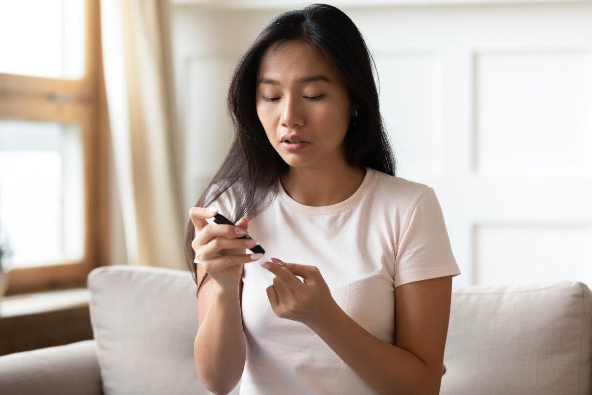woman with diabetes sits on couch pricking finger to measure blood sugar level at home