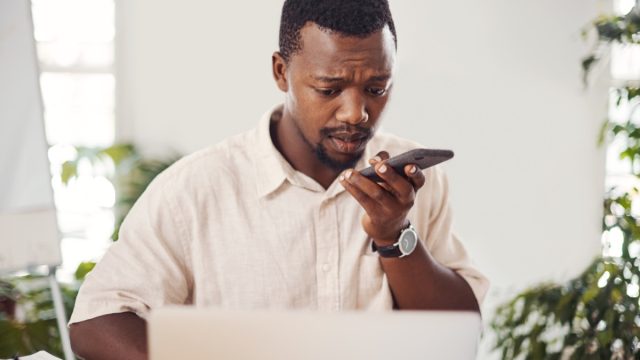 Shot of a young businessman talking on a cellphone while using a laptop in an office