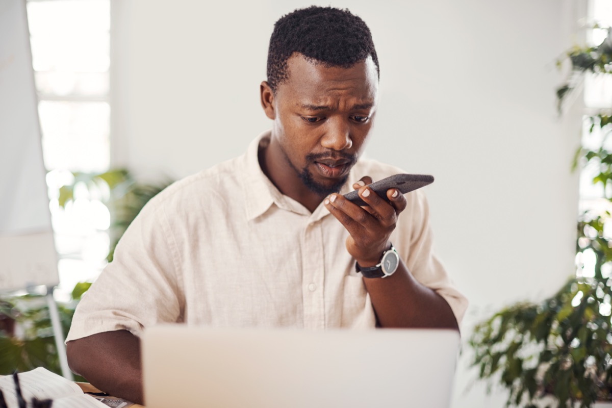 Shot of a young businessman talking on a cellphone while using a laptop in an office