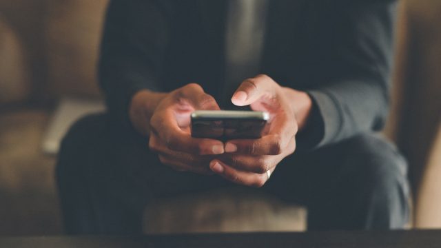 Cropped shot of an unrecognizable man using a smartphone while sitting indoors