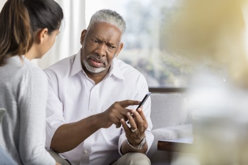 Man pointing at his cell phone and showing it to a younger woman