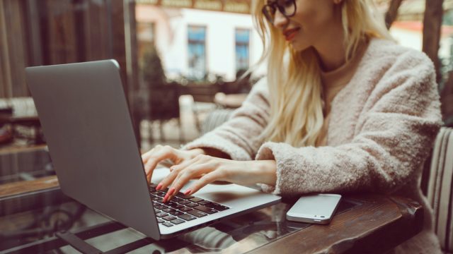 A young woman using an Apple MacBook laptop with an iPhone next to her