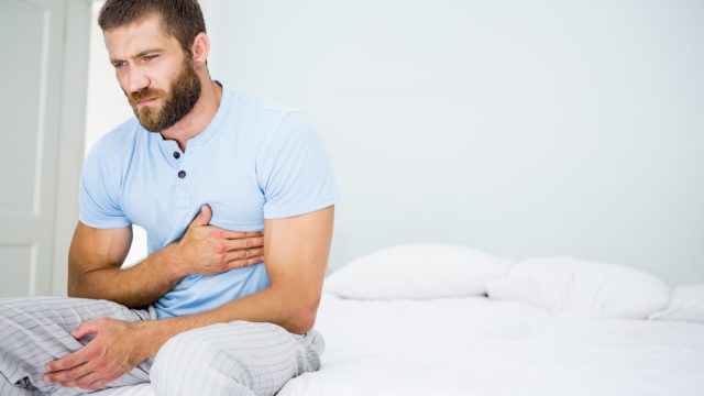 A young man sitting up in bed grabbing his chest with a pained look on his face