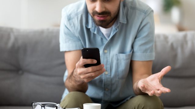 A man looking at his phone with a frustrated and confused look on his face, likely because it doesn't work