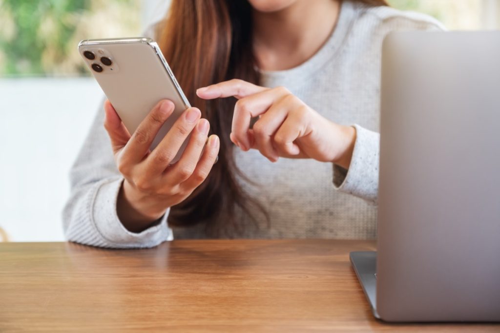 Jun 16th 2020 : A woman holding and using Iphone 11 Pro Max smart phone with Apple MacBook Pro laptop computer on wooden table , Chiang mai Thailand