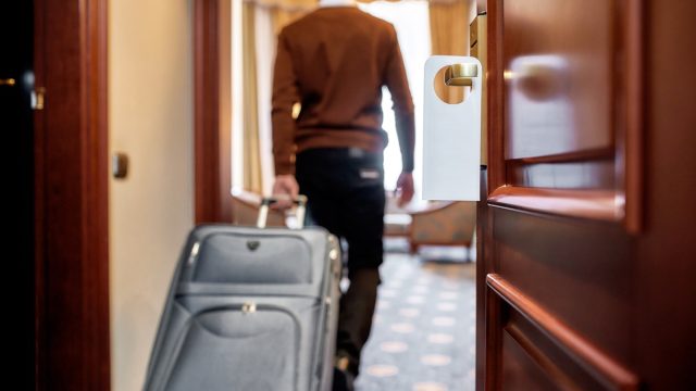 Cropped shot of middle-aged businessman in casual wear with suitcase entering his room in the background. A door with a sign at the front. Horizontal shot. Selective focus