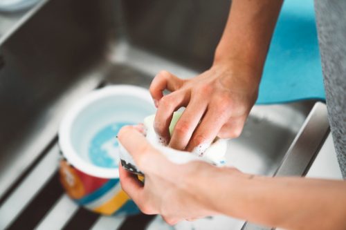 Unrecognizable woman hands washing dog bowl in the kitchen sink.