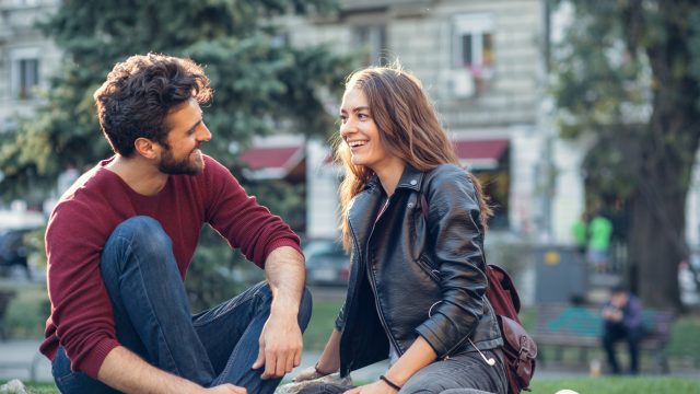 A young couple on a date sitting in a park chatting with each other and smiling