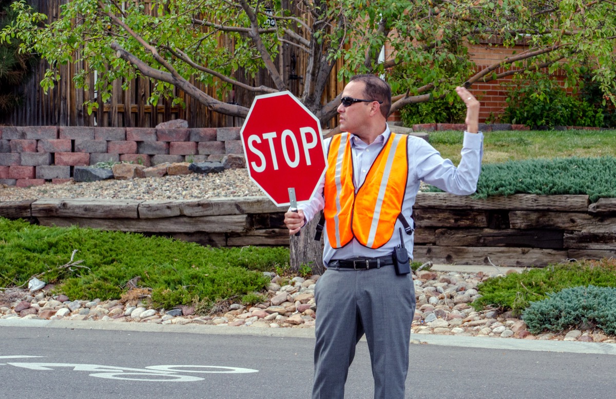 male crossing guard in orange vest gesturing to allow people across street