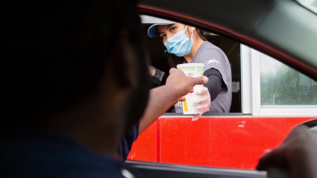 A man reaches for his food at the McDonalds drive-thru window as the employee wears a mask for protection.