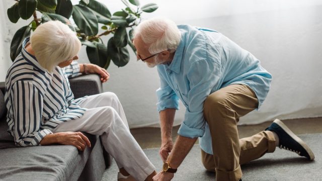 Side view of senior man lacing shoe of wife in living room