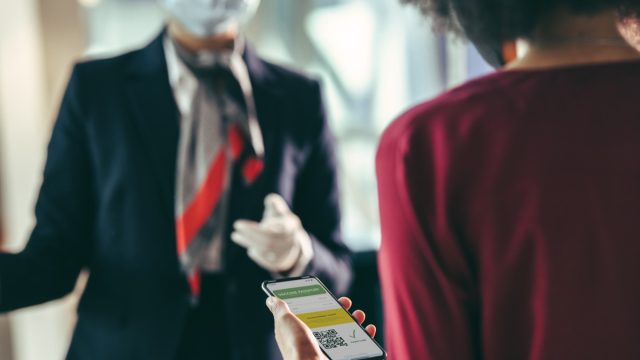 Female traveler holding mobile phone with vaccine passport at airport check-in counter. Woman passenger checking in at airport with her immunity passport during pandemic.