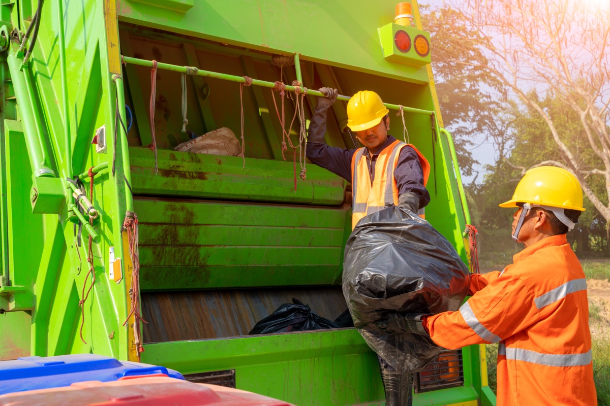 two garbage collectors loading black garbage bags into truck