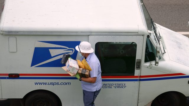 A mail carrier bringing boxes and envelopes from inside a mail truck