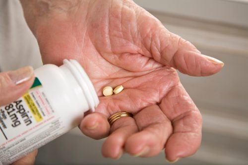 closeup of a senior person's hands taking two aspirin from the bottle